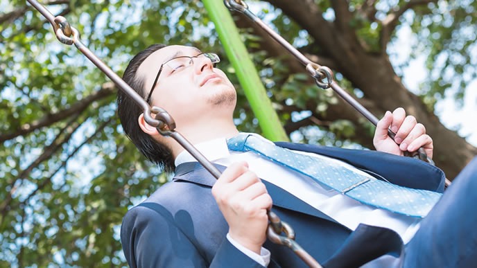 昼休みにさびしくブランコに乗る男性
