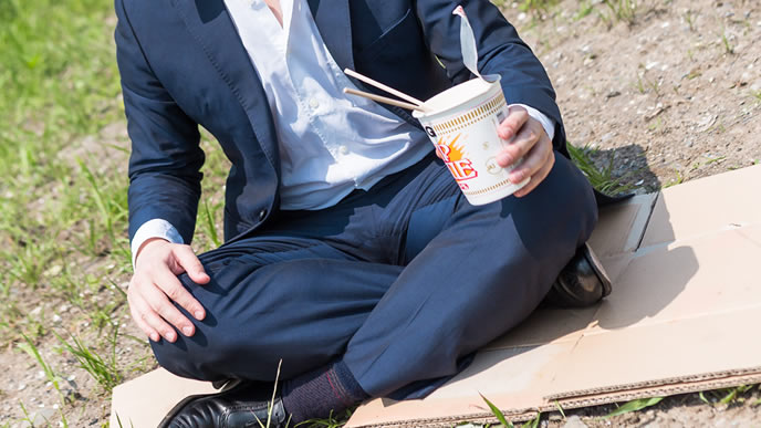 家がなく野原でラーメンを食べる男性