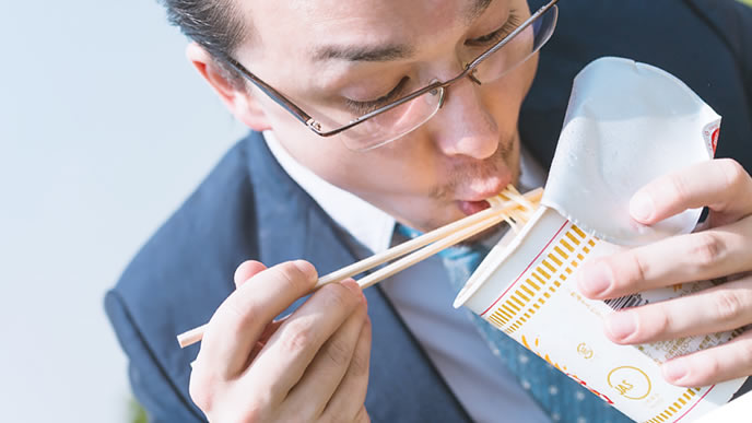 カップラーメンを食べて食費を節約する男性