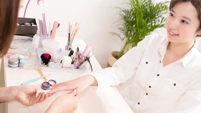 女性客の爪を拭きながら会話するネイリスト