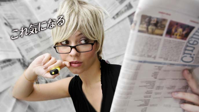 蛍光ペンを持って新聞を斜めに見つめる女性