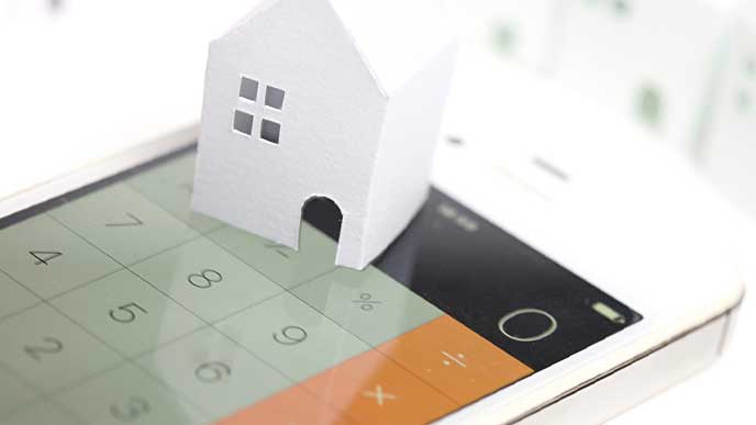 電卓アプリを表示しているスマホとペーパークラフトで作られた家