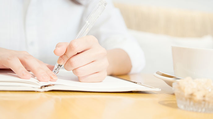 ノートをとる女性の手とコーヒーのカップ