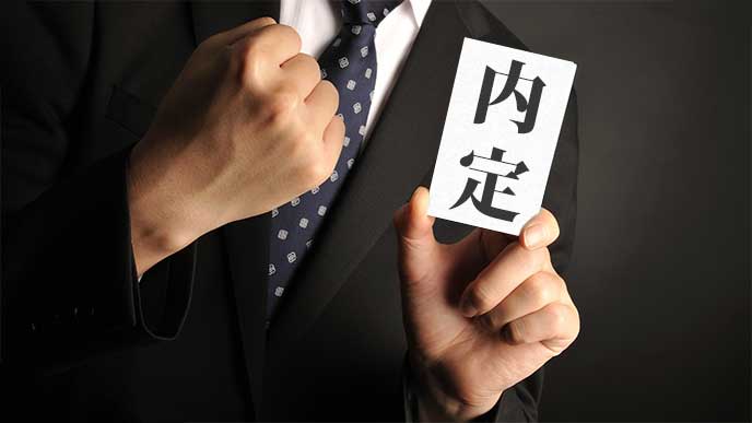 内定を手にしてガッツポーズのスーツを着た男性