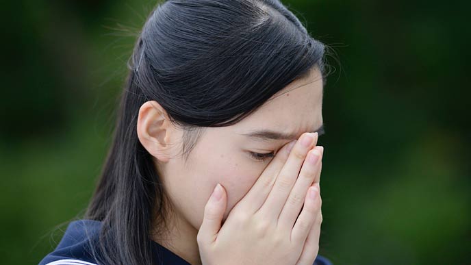 顔を手でおおう女子高生