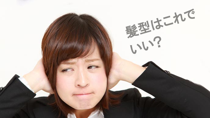 髪を両手で触るスーツ姿の女性