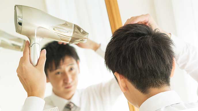 朝仕事に行くためにドライヤーを使ってヘアセットしてる男性