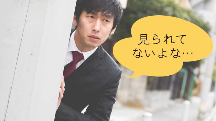 塀の後ろからコソコソ周りを気にする男性