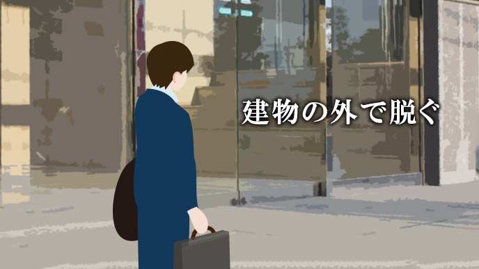 会社の玄関前でコートを脱ぐ就活学生