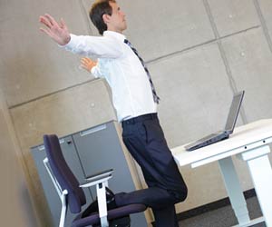 職場のデスクで片足で立つ休憩中の会社員