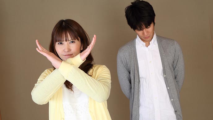 夫の前でバツサインを出す妻