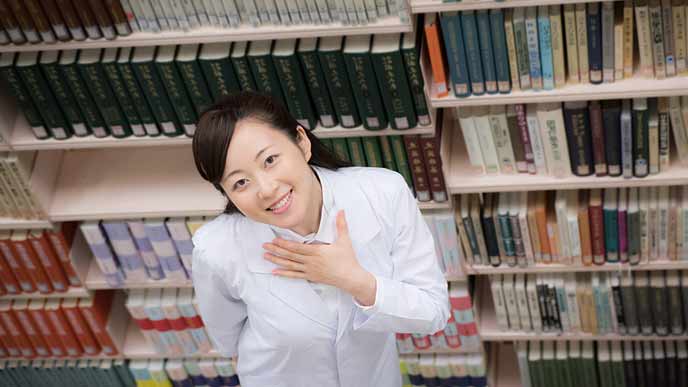 専門書の書棚の前に立つ大学院生