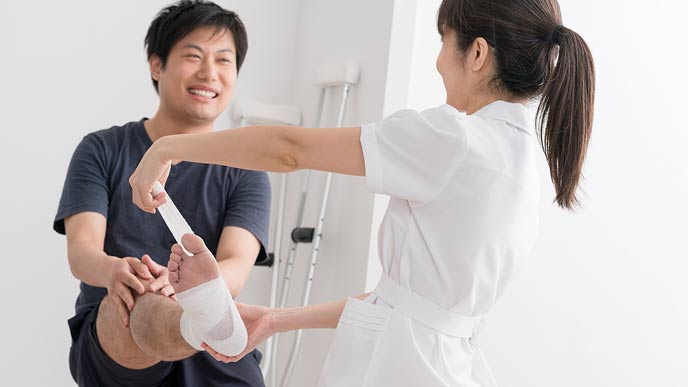 病院で足に包帯を巻かれる男性