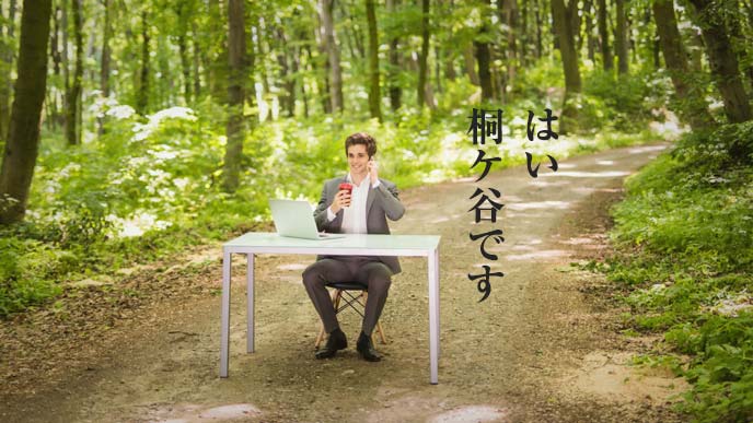 林道に置かれたパソコンデスクで電話に出る男性