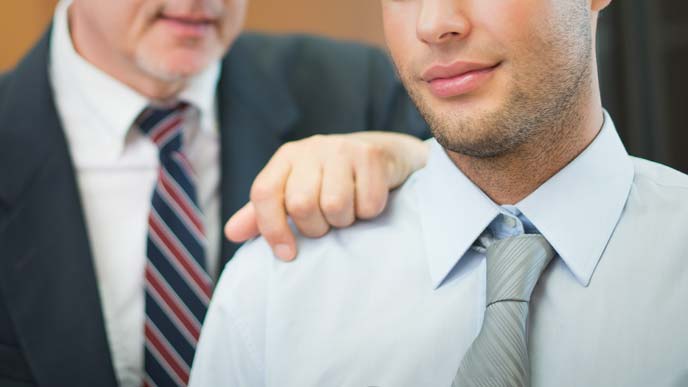 ホワイトカラーの男性の肩に手を置く年配の経営者