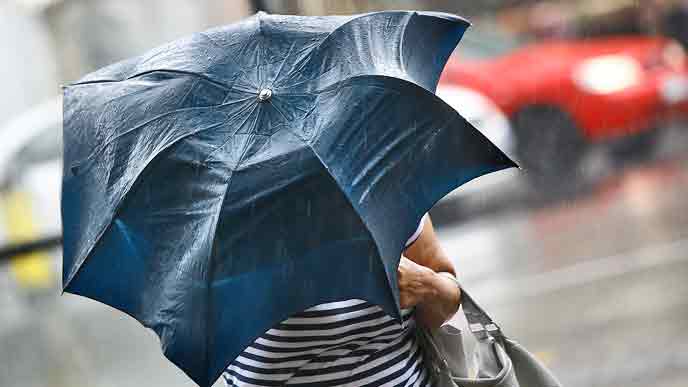 強い風雨で変形した傘をさして歩く人