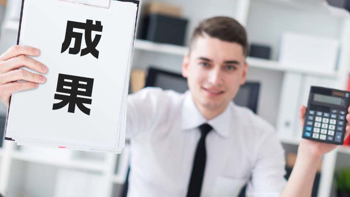 電卓を手に成果を掲げるスーツ姿の男子学生