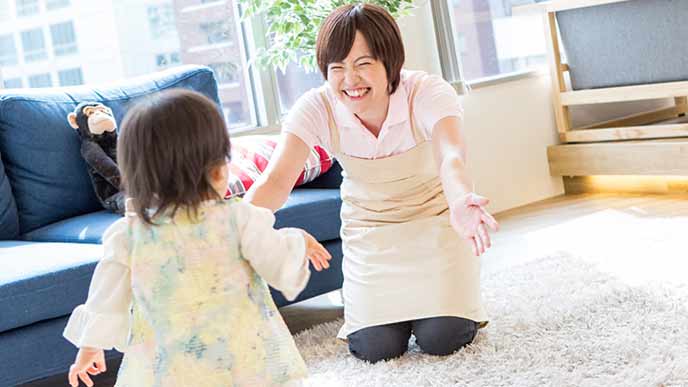 歩み寄る幼児に両腕を広げる笑顔の保育士